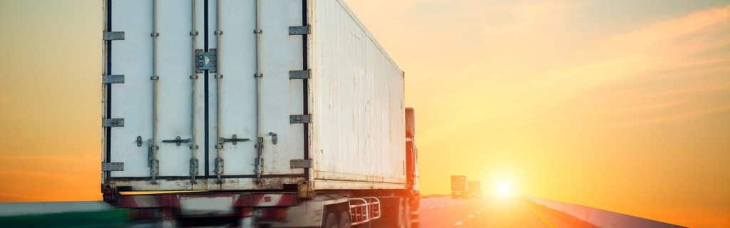 Rekka-auto kulkee tietä pitkin ja edessä kaunis auringonlasku.