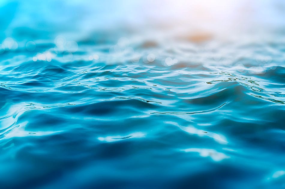 Vedenpinta, jossa pieniä laineita ja aurinko kimmeltää veden pinnalla.